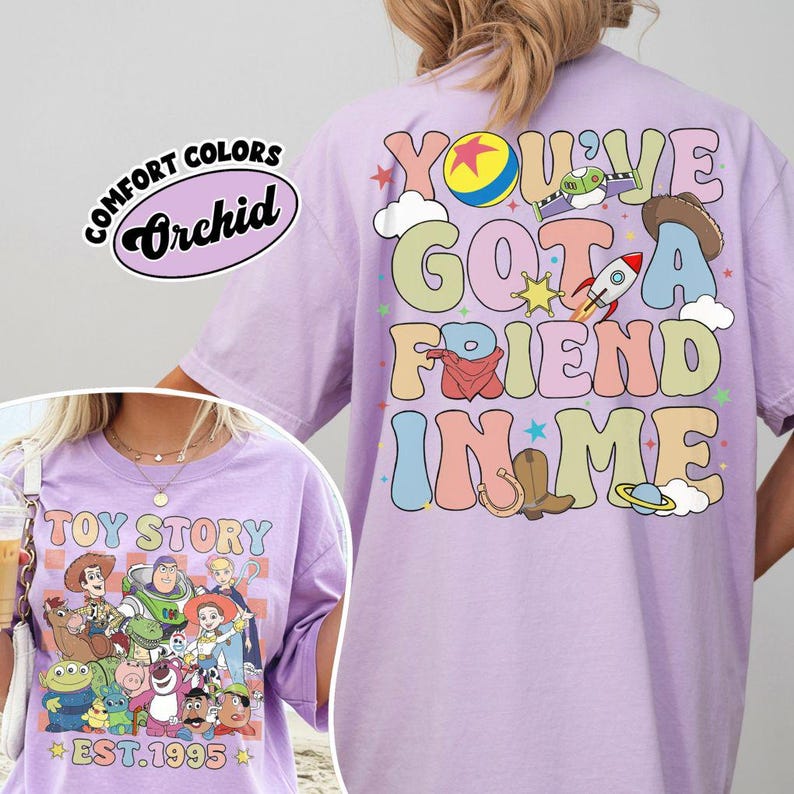 May include: A light purple t-shirt featuring a graphic from the movie Toy Story. The front of the shirt displays a group of characters with the text "TOY STORY EST. 1995". The back of the shirt has the phrase "YOU'VE GOT A FRIEND IN ME".