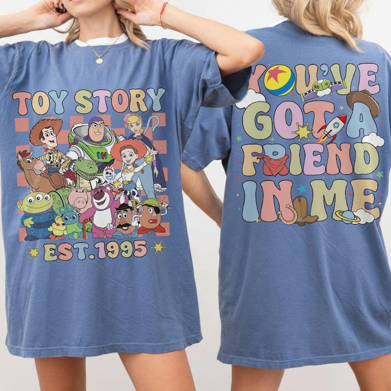 May include: Blue t-shirt featuring a colorful graphic of Toy Story characters with the text "TOY STORY EST. 1995" on the front. The back of the shirt has the phrase "YOU'VE GOT A FRIEND IN ME" in a retro font.