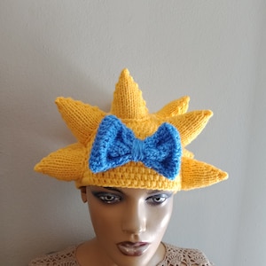 May include: A yellow knitted hat shaped like a sun with a blue knitted bow on top.