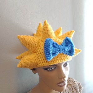 May include: A yellow knitted hat with a blue bow, shaped like a sun with pointy rays.