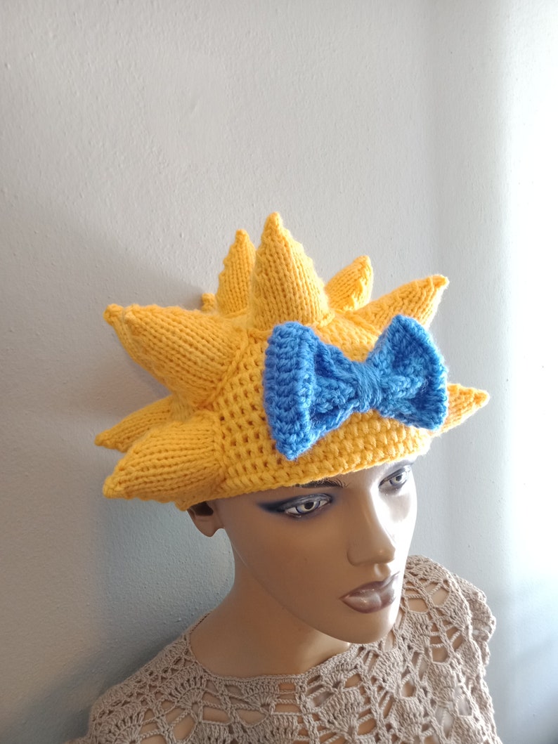 May include: A yellow knitted hat with a blue bow, shaped like a sun with pointy rays.