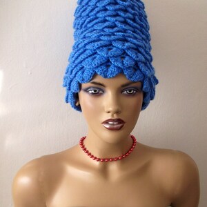 May include: A mannequin wearing a bright blue crocheted hat with a red beaded necklace. The hat is tall and has a unique, textured design.