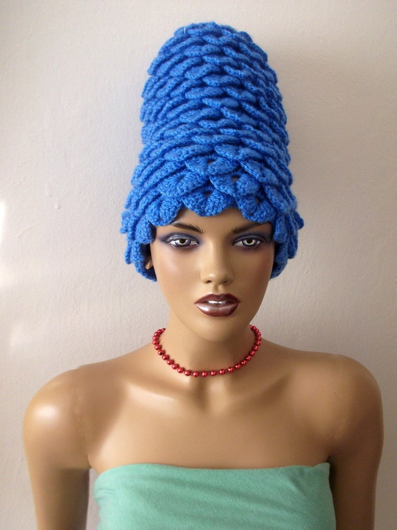 May include: A mannequin wearing a bright blue crocheted hat with a red beaded necklace. The hat is tall and has a unique, textured design.