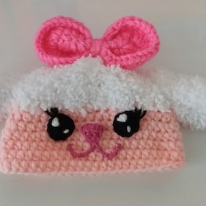 May include: A pink and white crocheted baby hat with a bow on top and a cute animal face. The hat has fluffy white ears.