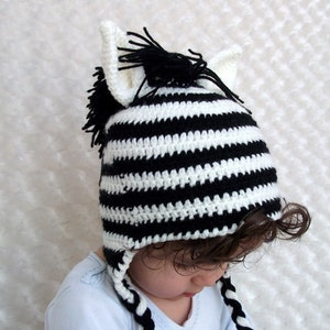 May include: A black and white striped crocheted zebra hat with long ear flaps and a black mane. The hat is worn by a child.