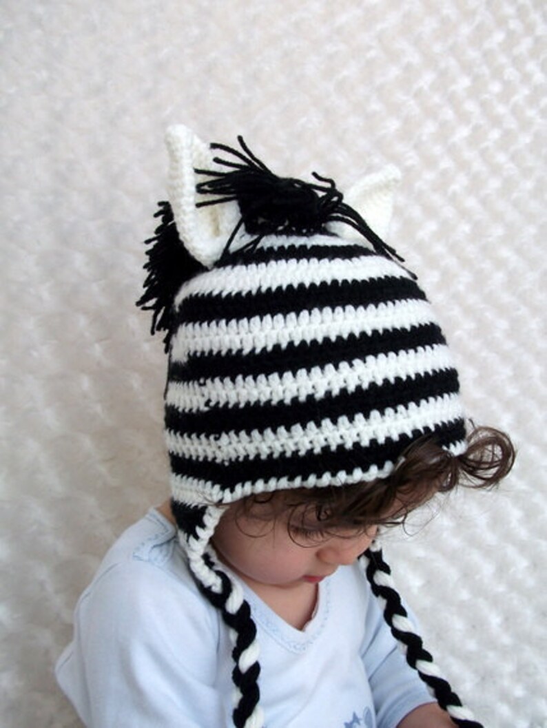 May include: A black and white striped crocheted zebra hat with long ear flaps and a black mane. The hat is worn by a child.