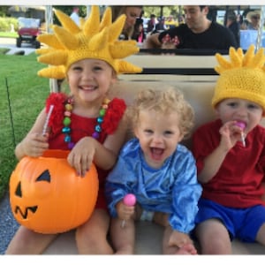 Könnte beinhalten: Drei Kinder in Halloween-Kostümen. Das Kind links trägt einen gelben Sonnenhut und ein rotes Kleid. Das Kind in der Mitte trägt ein blaues Hemd und hat blonde Haare. Das Kind rechts trägt einen gelben Sonnenhut und ein rotes Hemd. Alle drei Kinder halten Süßigkeiten.