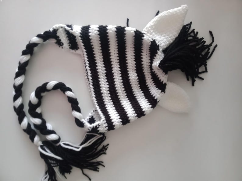 May include: Black and white striped crocheted zebra hat with a long tail and white ears.