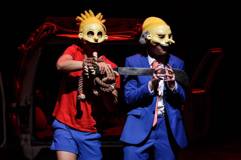 Puede incluir: Dos personas con m&aacute;scaras amarillas, una con camisa roja y pantalones cortos azules, la otra con traje azul, sosteniendo un cuchillo plateado.