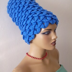 May include: A blue crocheted hat with a unique, textured design. The hat is worn by a mannequin with a red beaded necklace and a teal strapless top.