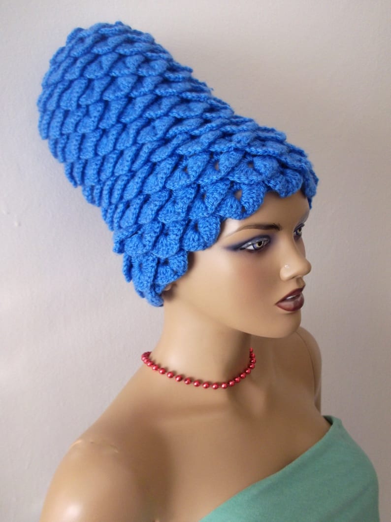 May include: A blue crocheted hat with a unique, textured design. The hat is worn by a mannequin with a red beaded necklace and a teal strapless top.