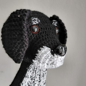 May include: A handmade black and white knitted dog head cover. The dog has brown eyes, a black nose, and white accents on the ears and muzzle. The cover is designed to fit over a golf club.