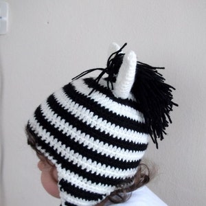 May include: A black and white striped crocheted zebra hat with a black pom-pom on top. The hat has long ear flaps.