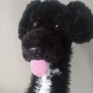 May include: A handmade plush dog puppet with black fur, brown eyes, and a pink tongue. The puppet has a white and black fluffy collar. The dog's nose is black and shiny. The puppet is designed to be held and used for play.