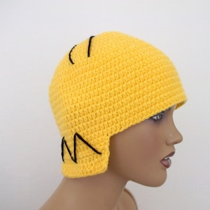 Peut inclure: Chapeau crocheté jaune avec des coutures noires formant un motif en zigzag sur les côtés. Le chapeau est porté sur une tête de mannequin.