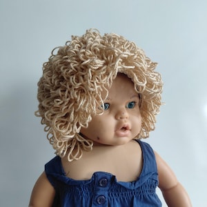 May include: A vintage doll with a light skin tone, blue eyes, and a slightly open mouth. The doll wears a blue dress and a curly, light-colored wig. The doll's features are detailed, and the overall aesthetic is reminiscent of classic toys.