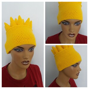 Puede incluir: Un gorro de punto amarillo con una parte superior puntiaguda, que se asemeja al cabello de un personaje de dibujos animados. El gorro lo lleva puesto un maniqu&iacute; con una camisa roja.