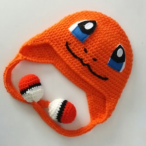May include: Orange crocheted hat with a cartoon face and two orange, white, and black crocheted balls attached to the hat's strings.