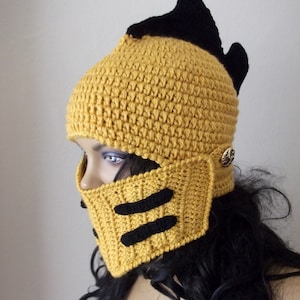 May include: A yellow crocheted hat with a black crocheted visor and a black crocheted spike on top. The hat has a black crocheted design on the visor.