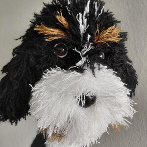 Puede incluir: Retrato de perro hecho a mano con hilo. El pelaje del perro es negro, blanco y dorado, con una barba blanca esponjosa y ojos oscuros. La obra de arte es un primer plano de la cara del perro, mostrando la textura del hilo.