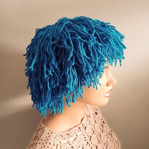 May include: A blue crocheted wig with long, shaggy strands. The wig is worn on a mannequin head with a crocheted top.