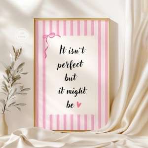 May include: A framed print with a gold border features the text "It isn't perfect but it might be" in black script. The background has pink and white vertical stripes, with a pink bow at the top. A small pink heart is at the bottom.