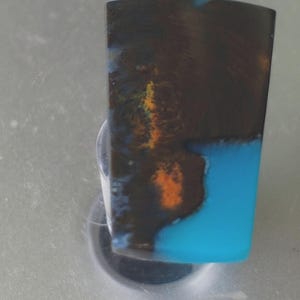 May include: A dark blue and brown cabochon with a bright turquoise blue section. The cabochon has a swirling pattern of colors and is set in a silver ring.