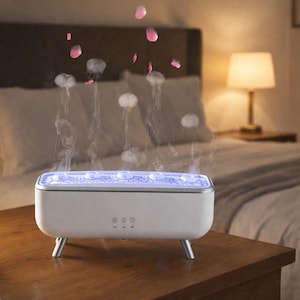 Op de afbeelding: Een witte aromatherapie diffuser met blauw licht. De diffuser staat op een houten nachtkastje, met een bed en lamp op de achtergrond. Stoom en roze bloemblaadjes stijgen op uit de diffuser.