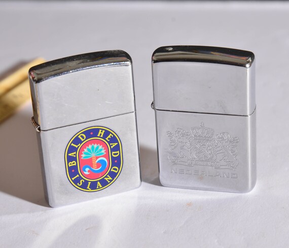Two vintage 1990s Zippo Lighters One Bald Head ISland and one Nederlands Netherlands Engraved