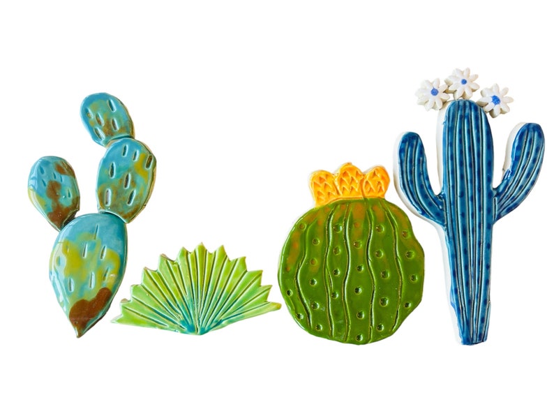 May include: A set of five ceramic cactus wall decor pieces. The set includes a tall blue cactus with white flowers, a round green cactus with a yellow crown, a green fan-shaped cactus, and two blue and green prickly pear cactus pieces.