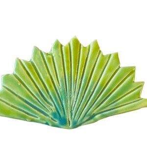 May include: A green and blue ceramic tile shaped like a fan with a textured surface.