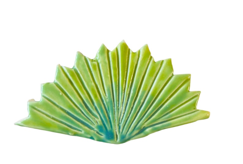 May include: A green and blue ceramic tile shaped like a fan with a textured surface.