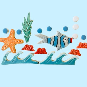 May include: Ceramic ocean-themed decorative pieces including a starfish, fish, waves, bubbles, and coral. The fish has blue and white stripes. The starfish is orange. The waves are blue and white.