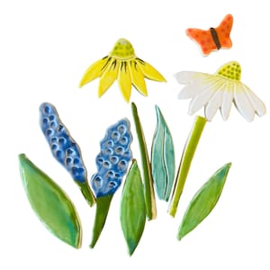 May include: Ceramic floral arrangement featuring a yellow flower, a white daisy, blue hyacinth-like blooms, green leaves, and an orange butterfly. The handcrafted art piece is set against a white background, showcasing the vibrant colors and textures of the ceramic elements.
