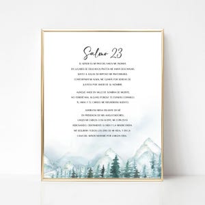以下が含まれることがあります： 「Salmo 23」のテキストが書かれた額入りのプリント。青と緑の色合いで描かれた山と木の水彩画の風景が特徴で、その下に詩篇のテキストが書かれています。フレームは金色です。