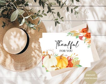 May include: A stack of white cards with the words "Thankful FOR YOU" in elegant script, featuring watercolor pumpkins and floral accents. A straw hat and beige blanket are in the background.