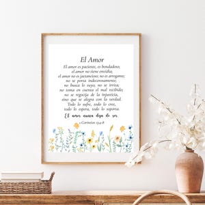 May include: A framed print with the text "El Amor" in Spanish, featuring a floral border of yellow and blue flowers. The text is a passage from 1 Corinthians 13:4-8. The frame is a light brown color.