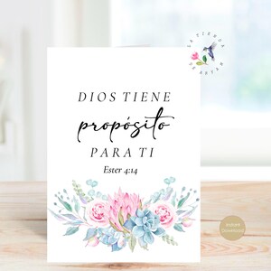 May include: A white card with the text "DIOS TIENE propósito PARA TI Ester 4:14" in black script. The card is decorated with watercolor flowers in pink, blue, and green. A small hummingbird logo is in the upper right corner.