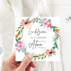May include: A square digital file with a floral wreath design. The wreath features pink and orange flowers with green leaves. Text in Spanish reads "La dulzura de la amistad fortalece el Alma" and "Proverbios 27:9". A small logo with a hummingbird is in the upper right corner.