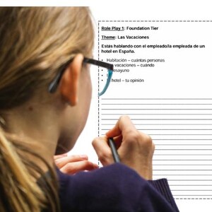 May include: A person is writing on a sheet of paper with lined paper. The paper has the title "Role Play 1: Foundation Tier" and the theme "Las Vacaciones". The text on the paper says "Estás hablando con el empleado/la empleada de un hotel en España." and lists the following topics: "Habitación - cuántas personas", "vacaciones - cuándo", "desayuno", and "hotel - tu opinión".