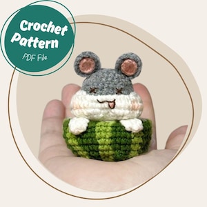 Op de afbeelding: Een handgemaakt gehaakt hamsterspeeltje met grijs en wit haar, roze wangen en een groen-wit gestreepte mand. De afbeelding bevat een cirkelvormige afbeelding met de tekst "Crochet Pattern PDF File."