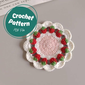 May include: A crochet coaster pattern featuring a white and pink circle with red and green strawberries around the edge. The pattern is available as a PDF file.
