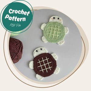 May include: Two crocheted turtle coasters, one brown and one green, with white accents. The coasters are on a light gray surface.