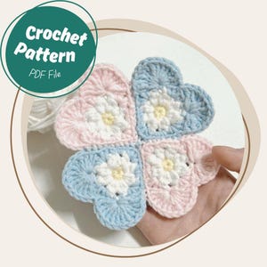 Puede incluir: Un diseño de trébol de cuatro hojas tejido a ganchillo en rosa y azul con centros de flores blancos y amarillos. La imagen incluye el texto "Crochet Pattern PDF File" en un círculo verde.