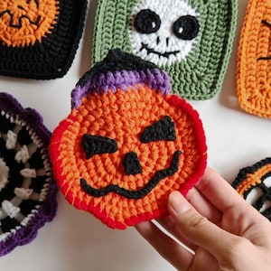 May include: Handmade crochet Halloween coasters in various designs. The coasters feature a pumpkin, skull, and other spooky motifs in orange, black, green, and purple. The coasters are square and round, perfect for adding a festive touch to any home.