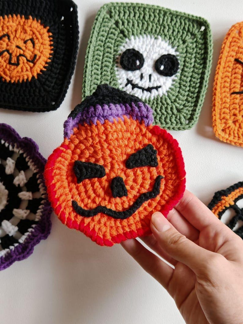 May include: Handmade crochet Halloween coasters in various designs. The coasters feature a pumpkin, skull, and other spooky motifs in orange, black, green, and purple. The coasters are square and round, perfect for adding a festive touch to any home.