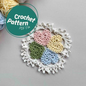May include: A crochet pattern PDF file for a colorful heart-shaped coaster. The coaster is made with white, pink, yellow, green, and blue yarn.