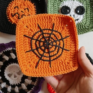 May include: Close-up of several crocheted Halloween-themed squares. One orange square features a black spiderweb design. Other squares include a black pumpkin, a green skull, and a purple and white design. The squares are handmade.