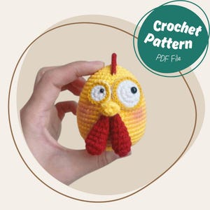 Könnte beinhalten: Ein handgehäkeltes Huhn in Gelb und Rot mit großen Kulleraugen und einem roten Kamm und Kehllappen. Das Huhn wird in einer Hand gehalten. Ein grüner Kreis mit dem Text "Crochet Pattern PDF File" befindet sich im Hintergrund.