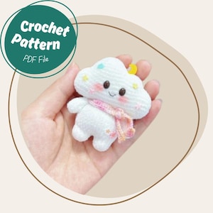May include: A handmade white crochet cloud-shaped plushie with a pink scarf, small arms and legs, and a smiling face. The cloud has a yellow crescent moon and blue and yellow accents. The image includes a green circle with the text "Crochet Pattern PDF File."
